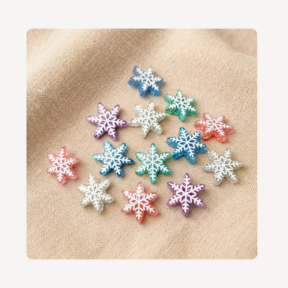 A group of small snowflake-shaped clog charms in assorted pastel and bright colors, arranged on a beige textured fabric background.