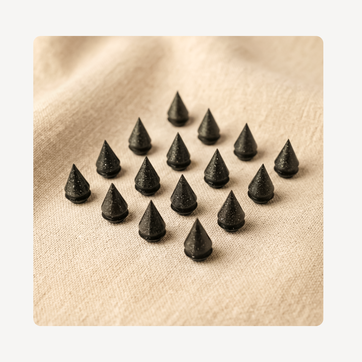 A set of small black cone-shaped clog charms arranged in rows on a beige textured fabric background.