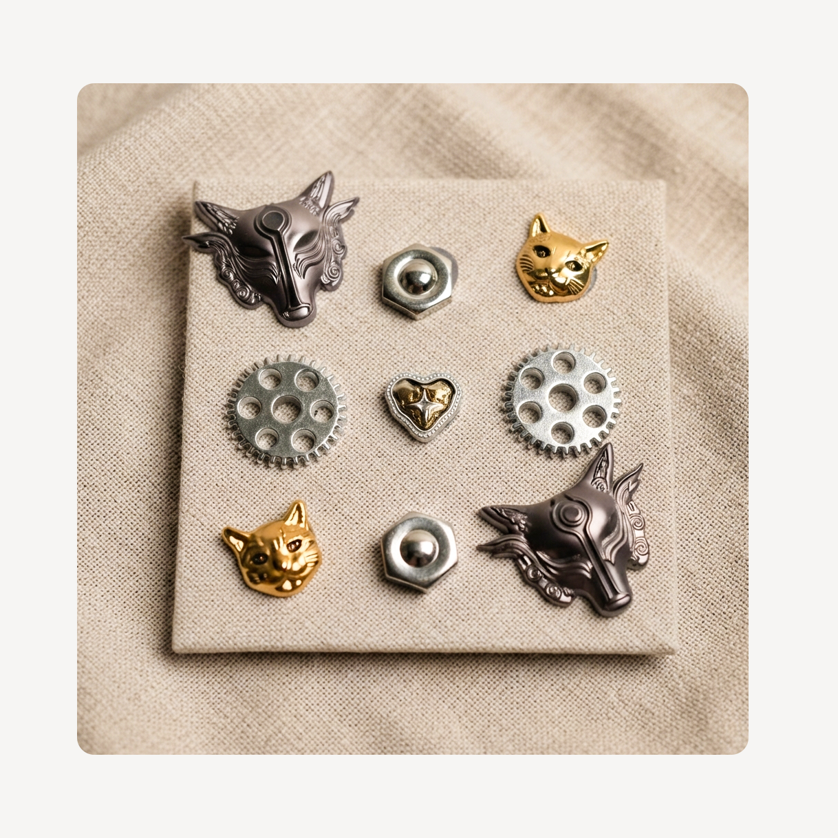 A set of nine clog charms displayed on a square beige fabric card. The set includes two silver wolf head charms, two gold cat head charms, three silver gear pieces, and three silver hex nuts.