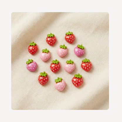 A set of 15 small strawberry-shaped clog charms arranged on a textured beige fabric background. The charms feature red and pink bodies with white seeds and green leafy tops.
