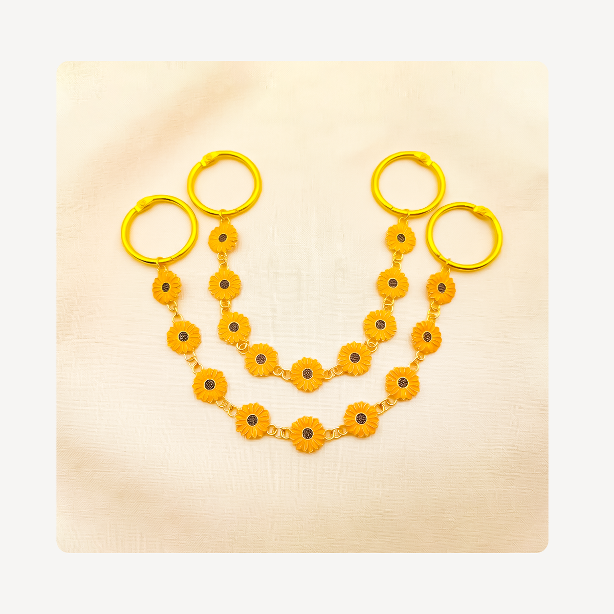 A pair of gold-toned clog chains with yellow flower charms, displayed on a light beige textured background.