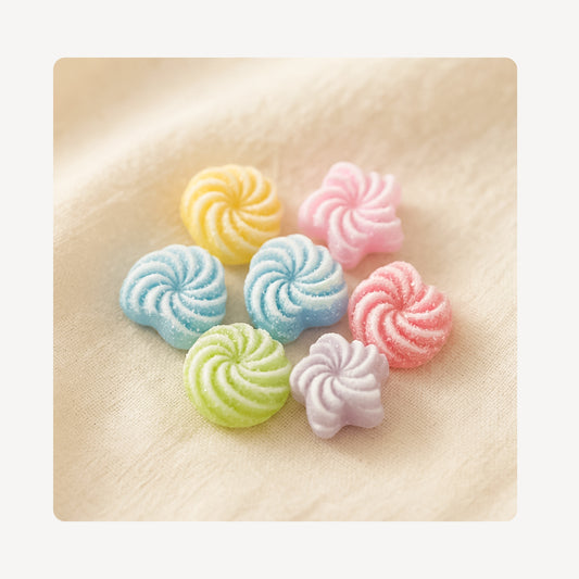 A top-down, square product thumbnail showing a collection of colorful, pastel swirled candy shoe charms arranged neatly on a soft, neutral-colored linen fabric background.
