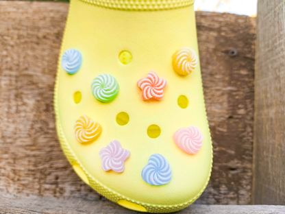 A bright yellow clog-style shoe decorated with colorful spiral-shaped resin candy charms, photographed against a rustic wooden background.