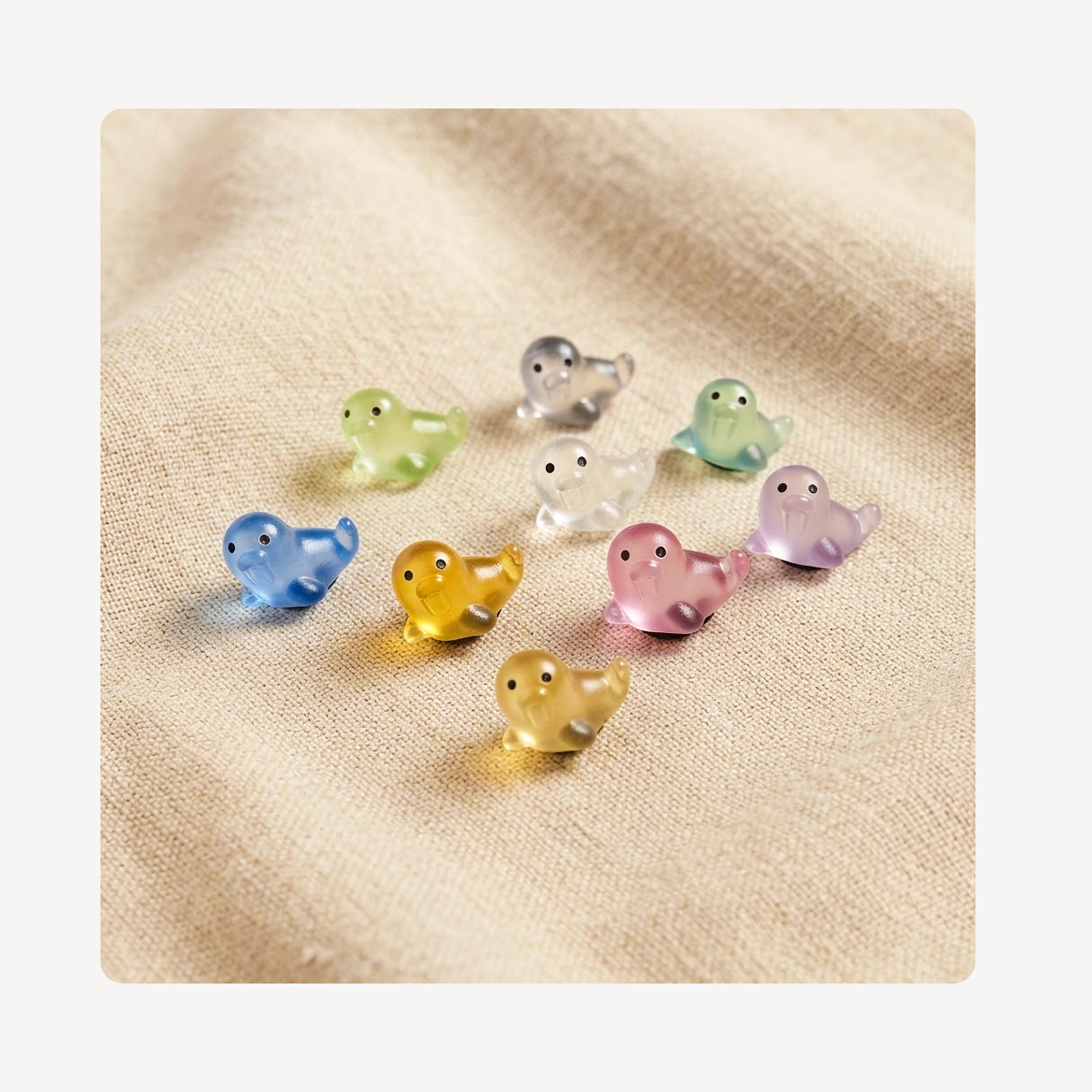 A set of nine small, translucent walrus clog charms in various pastel and neutral colors, arranged on a textured beige fabric background.