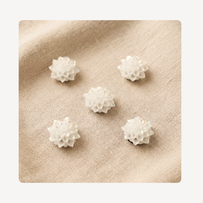 Five small white textured flower-shaped clog charms arranged on a beige linen fabric background.