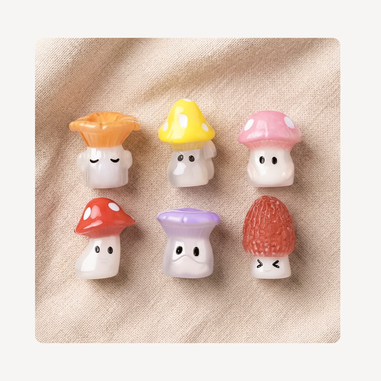 Six small mushroom-shaped clog charms arranged in two rows on a beige textured fabric background. The mushrooms have white faces and caps in orange, yellow, pink, red, and purple, with one having a textured red cap.
