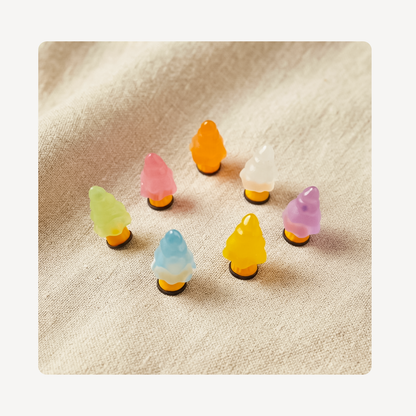 Seven small translucent tree-shaped clog charms in pastel colors arranged on a beige textured fabric background.