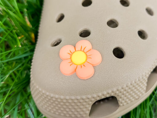A cluster of vibrant cosmos flower charms decorates a Crocs shoe, with each charm showcasing delicate petals in shades of pink, white, and purple. The intricate details of the flowers mimic real cosmos blooms, with soft gradients and textured centers