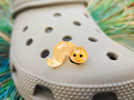A collection of glow worm caterpillar croc charms attached to a single Croc shoe. The charms feature caterpillar designs in various bright colors, including green, yellow, blue, pink, and orange, all designed to glow in the dark.