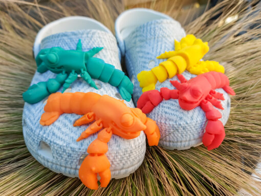 Colorful 3D printed flexi lobster charms in green, orange, yellow, and red, attached to Crocs shoes. Each lobster has a segmented, flexible body and realistic details, adding a playful marine-inspired style to the shoes.