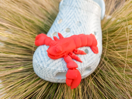 Colorful 3D printed flexi lobster charms in green, orange, yellow, and red, attached to Crocs shoes. Each lobster has a segmented, flexible body and realistic details, adding a playful marine-inspired style to the shoes.