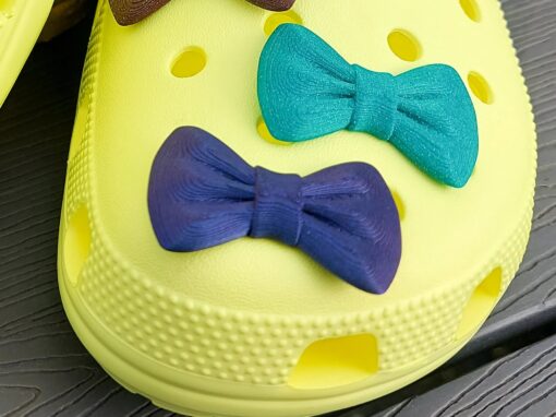 3d-printed bow shoe charms on a pair of Crocs shoes. Multiple colors and they have a sparkly glitter.