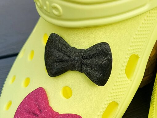 3d-printed bow shoe charms on a pair of Crocs shoes. Multiple colors and they have a sparkly glitter.