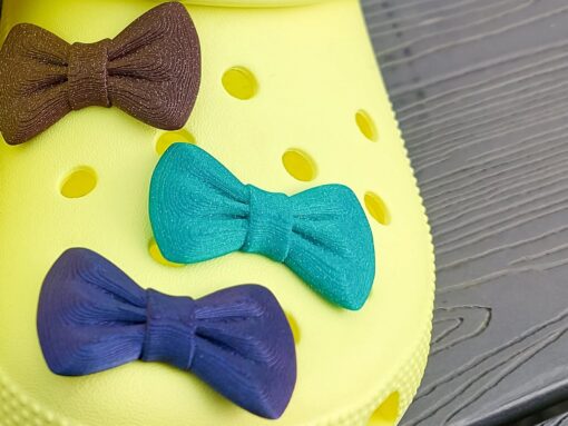 3d-printed bow shoe charms on a pair of Crocs shoes. Multiple colors and they have a sparkly glitter.