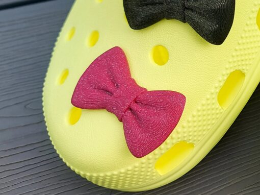 3d-printed bow shoe charms on a pair of Crocs shoes. Multiple colors and they have a sparkly glitter.