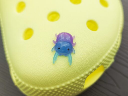 A vibrant collection of beetle-themed Croc charms decorates a yellow Crocs shoe. The charms feature detailed, multicolored beetles in various shades, adding a playful yet nature-inspired vibe to the footwear.