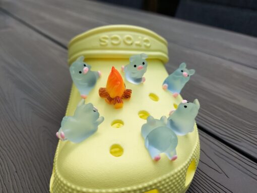 Set of glow-in-the-dark Croc charms featuring adorable pigs around a campfire on a Croc shoe. These playful accessories light up in the dark, adding a unique and whimsical touch to your footwear, perfect for personalizing your Crocs.