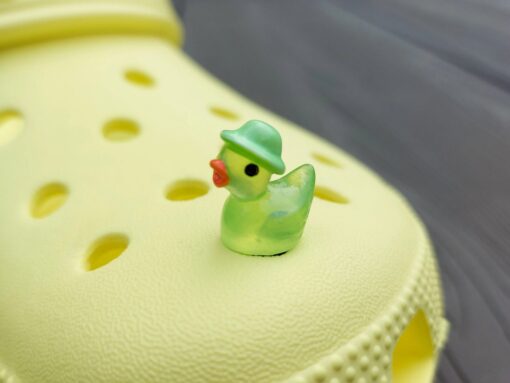 Glow in the dark duck charms wearing bucket hats on a yellow Crocs shoe. These colorful charms are available in pink, white, blue, green, yellow, turquoise, peach and purple. The hats all have different colors.