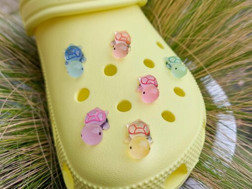 Glow-in-the-dark turtle charms on a Croc shoe. These adorable accessories, featuring detailed shell designs, bring a playful and luminous touch to the footwear, perfect for customizing your Crocs with a fun, ocean-inspired look.