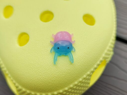 A vibrant collection of beetle-themed Croc charms decorates a yellow Crocs shoe. The charms feature detailed, multicolored beetles in various shades, adding a playful yet nature-inspired vibe to the footwear.