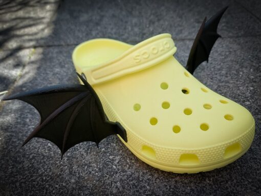 3d-printed bat or dragon wings shoe charms on a pair of Crocs shoes. They look halloween themed.