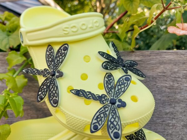 3D-printed glow-in-the-dark dragonfly charm with a Celtic weave pattern on a Croc shoe. The intricate design adds a whimsical and enchanting touch to the footwear, perfect for day or night style.