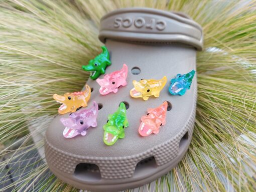 A set of glow-in-the-dark crocodile charms adorns a Crocs shoe. Each charm is shaped like a small, detailed crocodile, appearing in a range of bright colors that glow vividly in the dark.