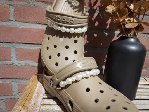 Close-up of a white pearl chain charm on a pair of Crocs, featuring a string of lustrous pearls elegantly draped across the shoe. The charm adds a classic and timeless touch to the footwear, creating a sophisticated and luxurious look.