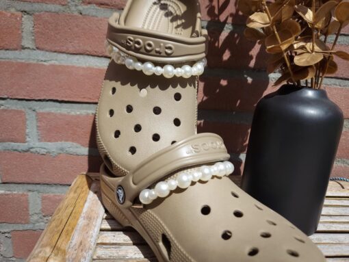 Close-up of a white pearl chain charm on a pair of Crocs, featuring a string of lustrous pearls elegantly draped across the shoe. The charm adds a classic and timeless touch to the footwear, creating a sophisticated and luxurious look.