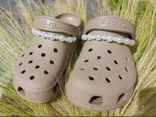 Close-up of a white pearl chain charm on a pair of Crocs, featuring a string of lustrous pearls elegantly draped across the shoe. The charm adds a classic and timeless touch to the footwear, creating a sophisticated and luxurious look.