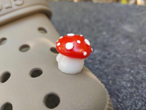 Glow in the dark forest mushroom shoe charms with white stems and red caps with white dots on a pair of Crocs shoes.