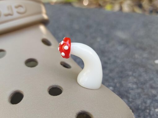 Glow in the dark forest mushroom shoe charms with white stems and red caps with white dots on a pair of Crocs shoes.