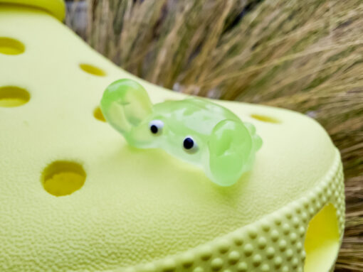 Close-up of a yellow Croc shoe adorned with colorful glow-in-the-dark crab charms in various shades. The charms have cute, detailed faces and are displayed in vibrant colors, ready to glow once charged under sunlight.