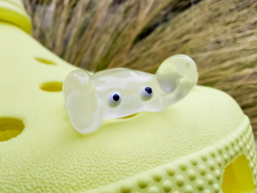 Close-up of a yellow Croc shoe adorned with colorful glow-in-the-dark crab charms in various shades. The charms have cute, detailed faces and are displayed in vibrant colors, ready to glow once charged under sunlight.