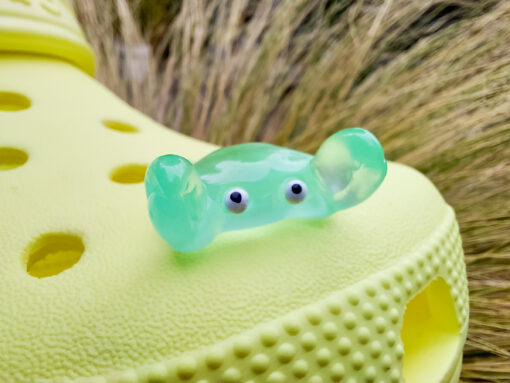 Close-up of a yellow Croc shoe adorned with colorful glow-in-the-dark crab charms in various shades. The charms have cute, detailed faces and are displayed in vibrant colors, ready to glow once charged under sunlight.