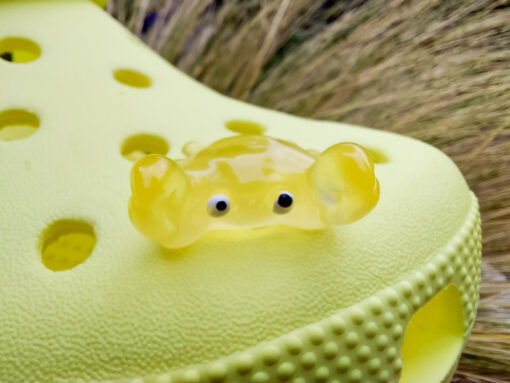 Close-up of a yellow Croc shoe adorned with colorful glow-in-the-dark crab charms in various shades. The charms have cute, detailed faces and are displayed in vibrant colors, ready to glow once charged under sunlight.