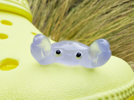 Close-up of a yellow Croc shoe adorned with colorful glow-in-the-dark crab charms in various shades. The charms have cute, detailed faces and are displayed in vibrant colors, ready to glow once charged under sunlight.