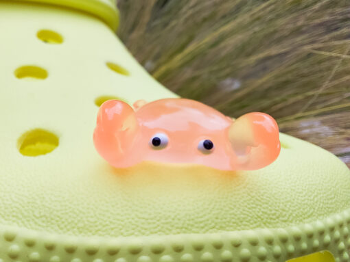 Close-up of a yellow Croc shoe adorned with colorful glow-in-the-dark crab charms in various shades. The charms have cute, detailed faces and are displayed in vibrant colors, ready to glow once charged under sunlight.