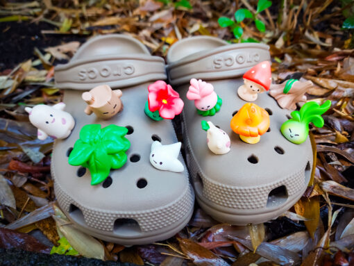 A tan Crocs shoe adorned with an 11-piece enchanted forest set featuring magical creatures, mushrooms, and plants, set against a backdrop of brown, wet leaves for a whimsical nature-inspired look.