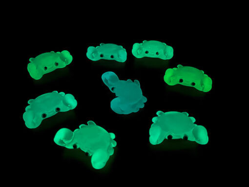 Close-up of a yellow Croc shoe adorned with colorful glow-in-the-dark crab charms in various shades. The charms have cute, detailed faces and are displayed in vibrant colors, ready to glow once charged under sunlight.