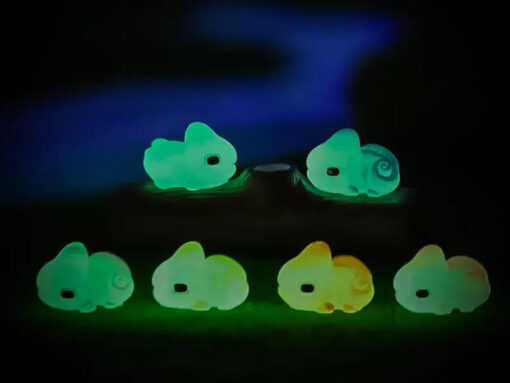 A close-up of a yellow Croc shoe with vibrant glow-in-the-dark chameleon charms in different colors (green, orange, pink, blue, and yellow) displayed outdoors on green grass.