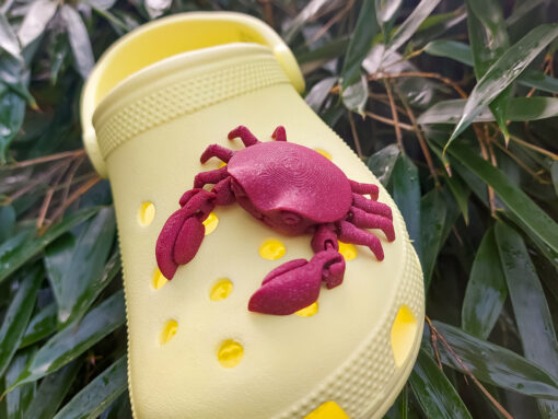 A 3D-printed, flexible red crab charm attached to a yellow Croc shoe. The crab charm features articulated claws and realistic texture, adding a fun and beach-inspired touch to the footwear. Perfect for ocean lovers and those seeking unique shoe accessories.