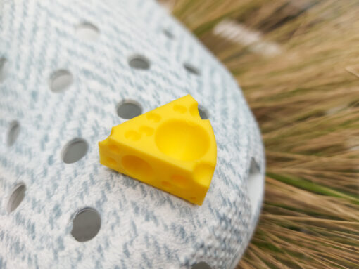 Close-up of a pair of light blue shoes decorated with colorful 3D-printed cheese wedge charms in shades of yellow, orange, and pink. The cheese charms feature realistic holes and a playful, quirky design, adding a fun pop of color to the footwear.