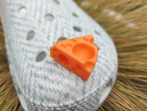Close-up of a pair of light blue shoes decorated with colorful 3D-printed cheese wedge charms in shades of yellow, orange, and pink. The cheese charms feature realistic holes and a playful, quirky design, adding a fun pop of color to the footwear.